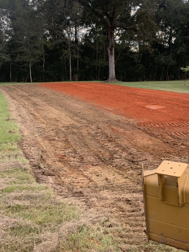A bulldozer is moving dirt in a field with trees in the background.