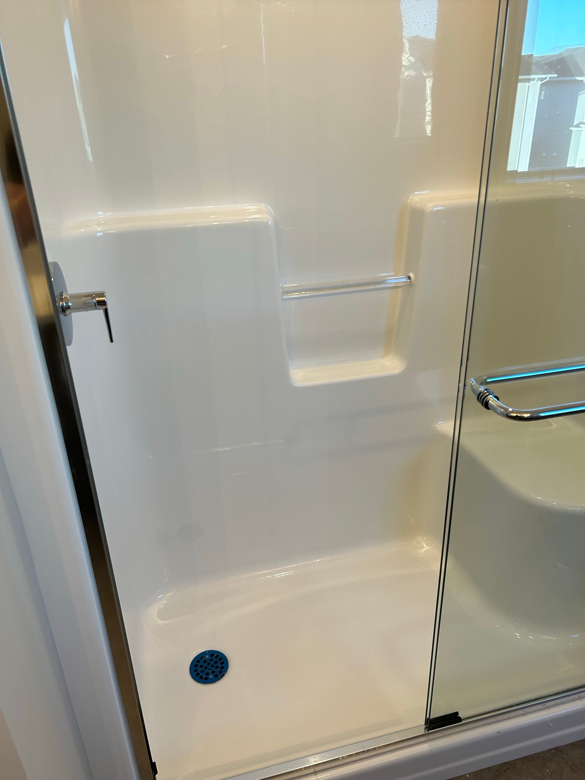 A white shower stall with a glass door and a blue drain.