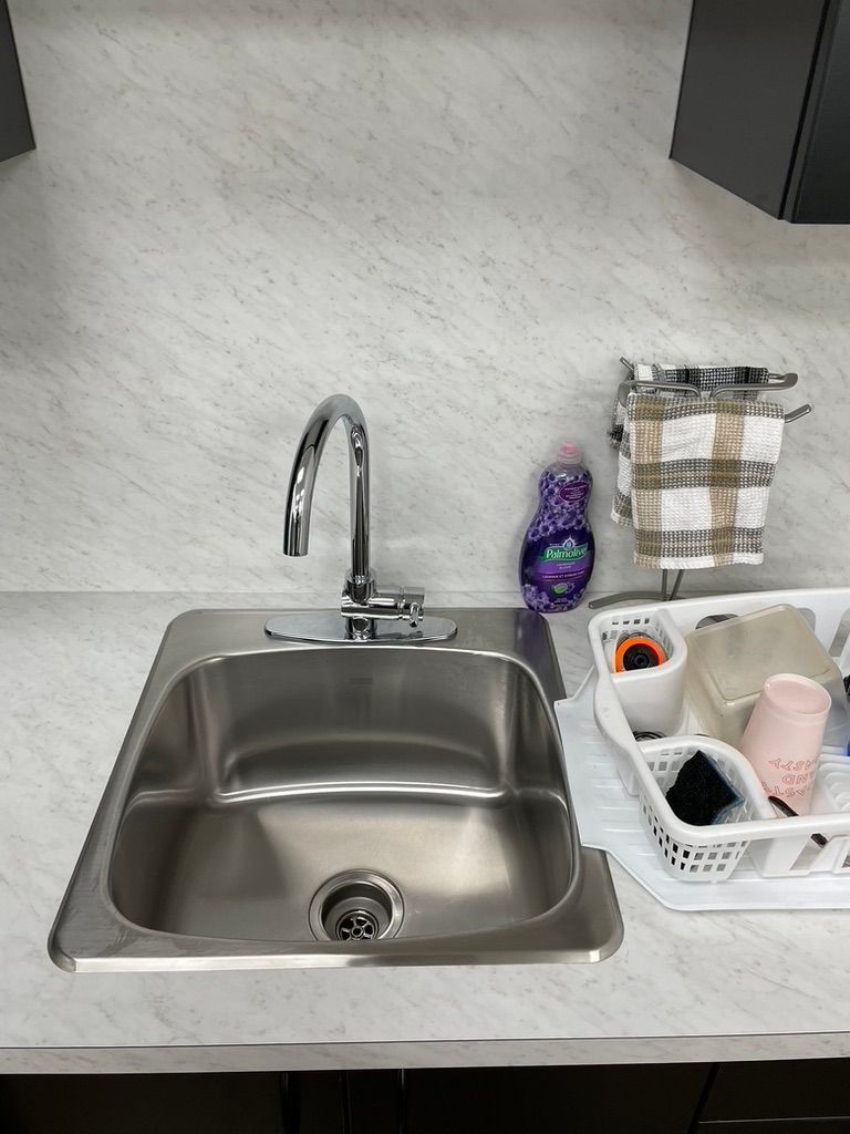 A stainless steel kitchen sink with a faucet and a basket of dishes on the counter.