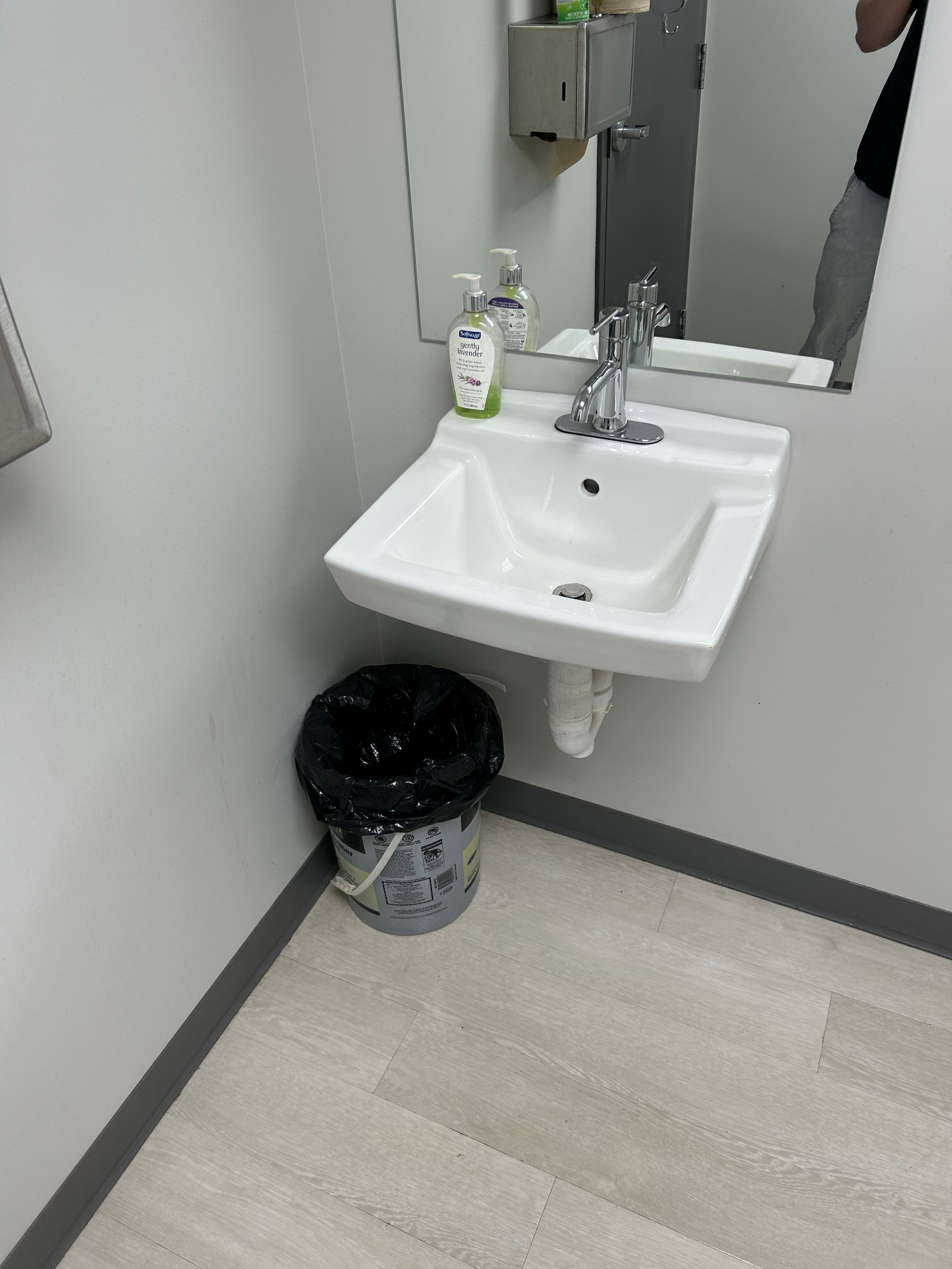 A bathroom with a sink , mirror and trash can