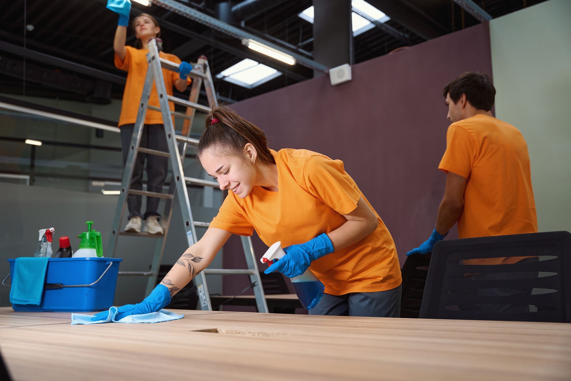 A woman is cleaning a wooden table in an office.
