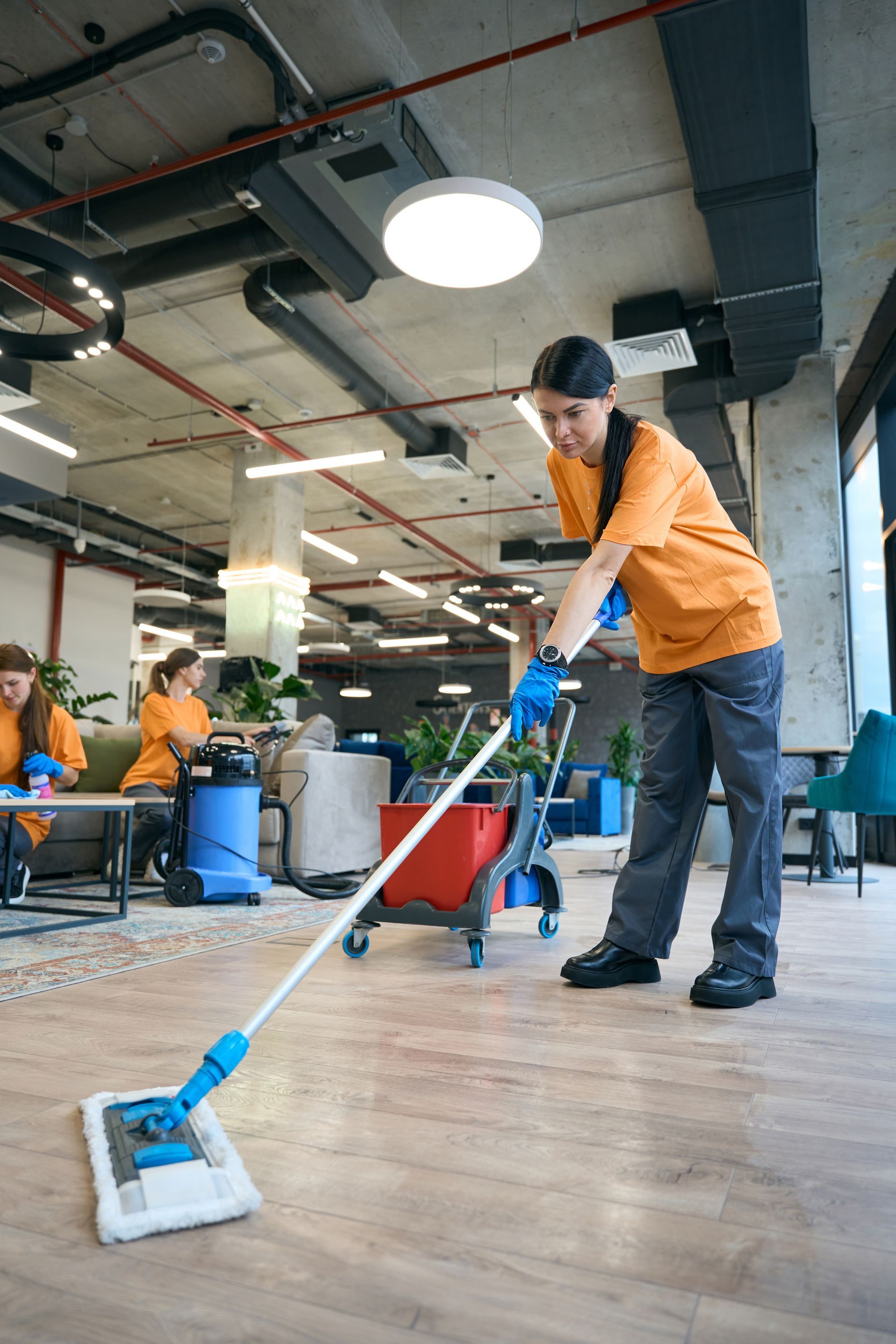 A woman is cleaning the floor of an office with a mop.