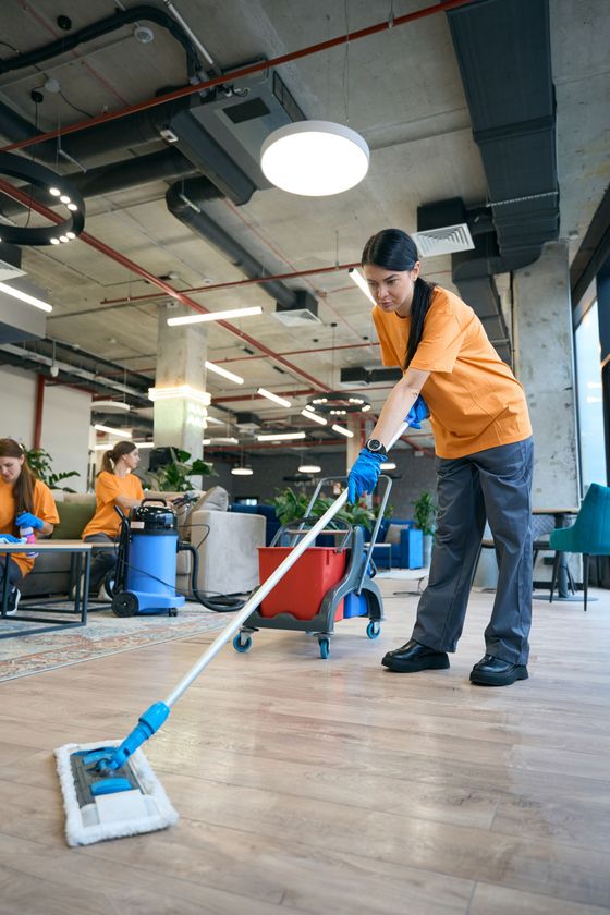 A woman is cleaning the floor of an office with a mop.