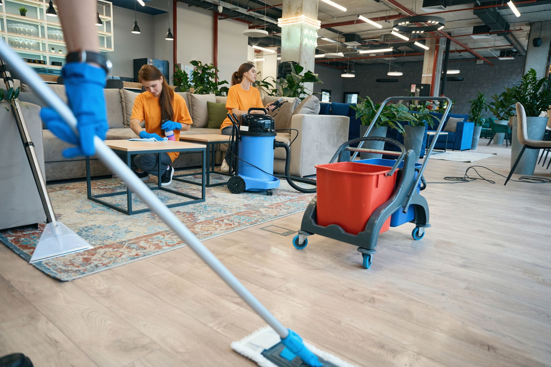 A woman is cleaning the floor of an office with a mop.