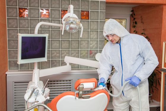 A man in a protective suit is cleaning a dental chair in a dental office.