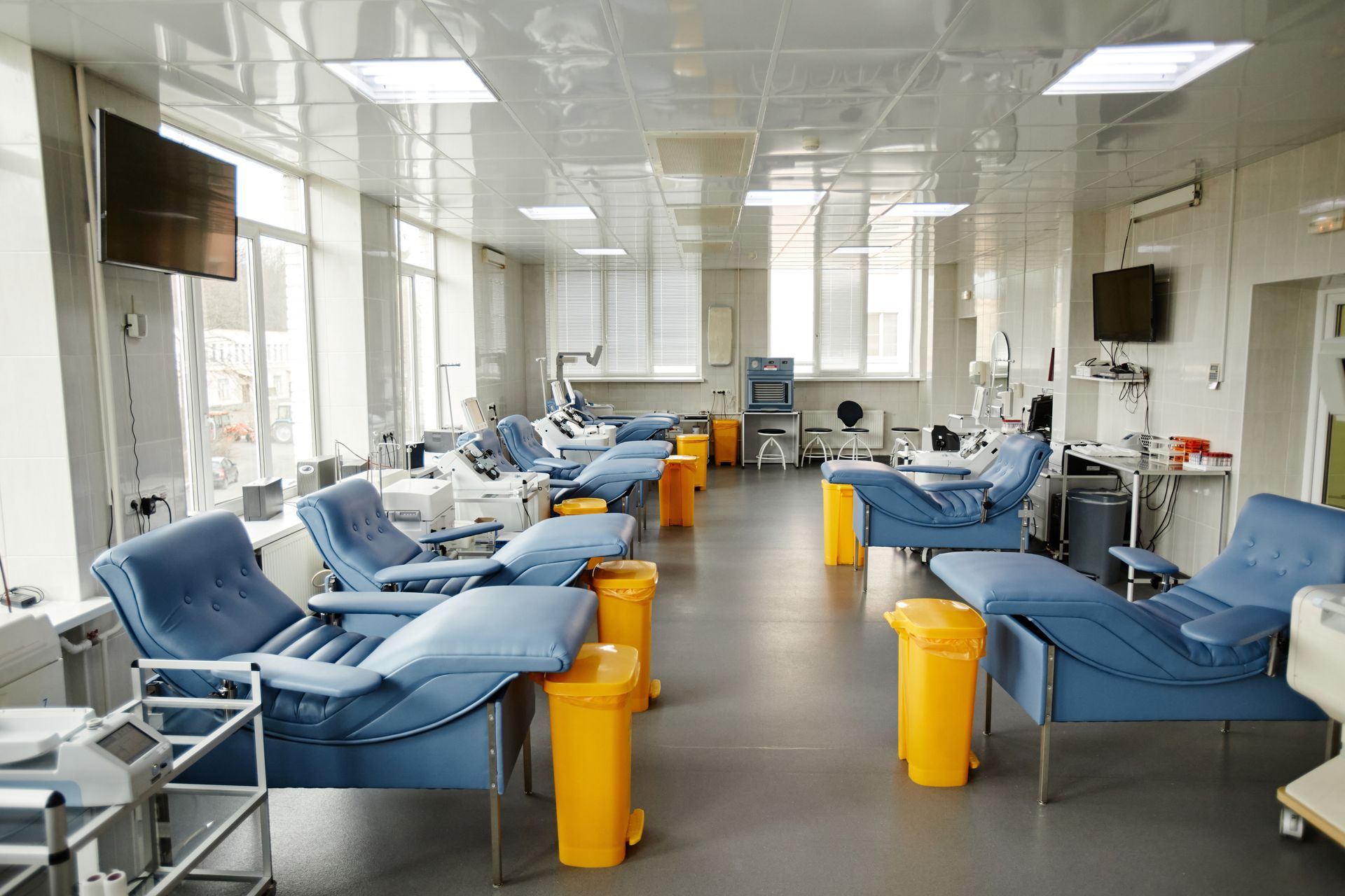 A room filled with lots of chairs and yellow trash cans in a hospital.