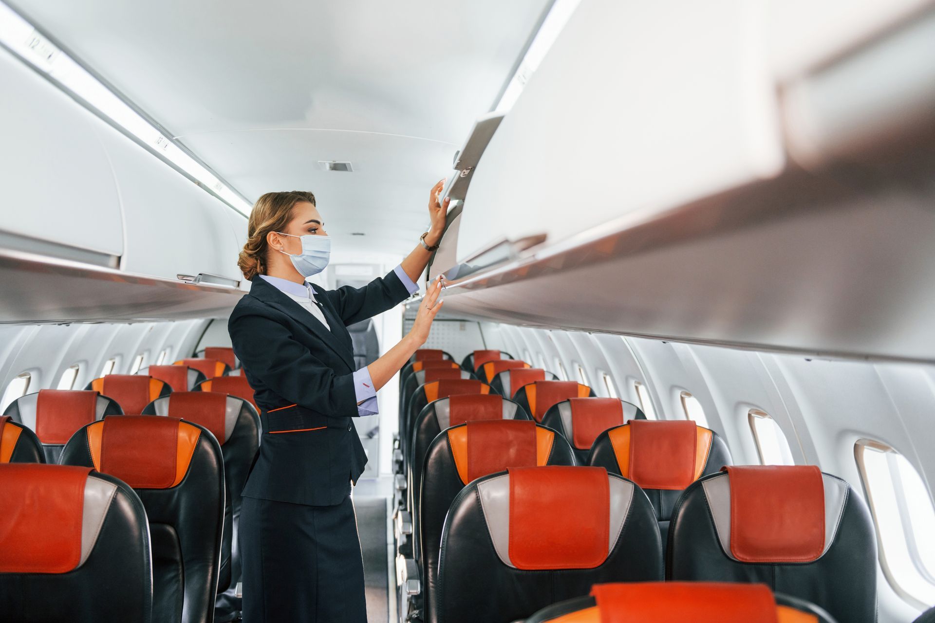 A flight attendant wearing a mask is standing in an airplane.
