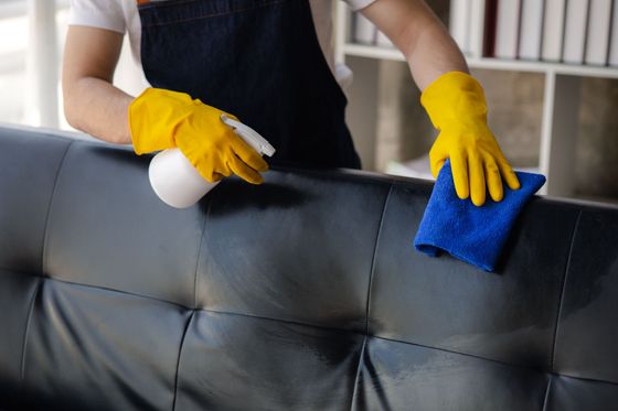 A person wearing yellow gloves is cleaning a black leather couch.