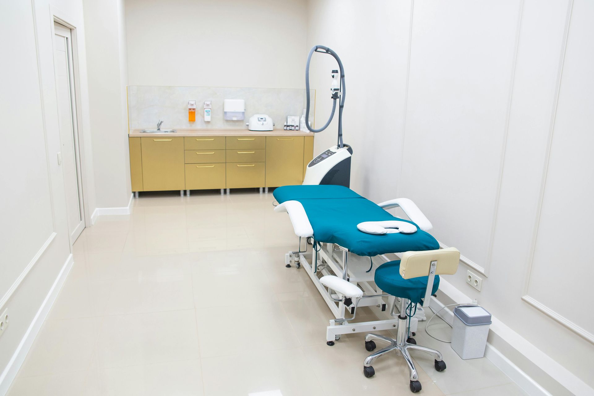 Examination room with medical equipment, beige cabinets, teal exam table, and laser machine.