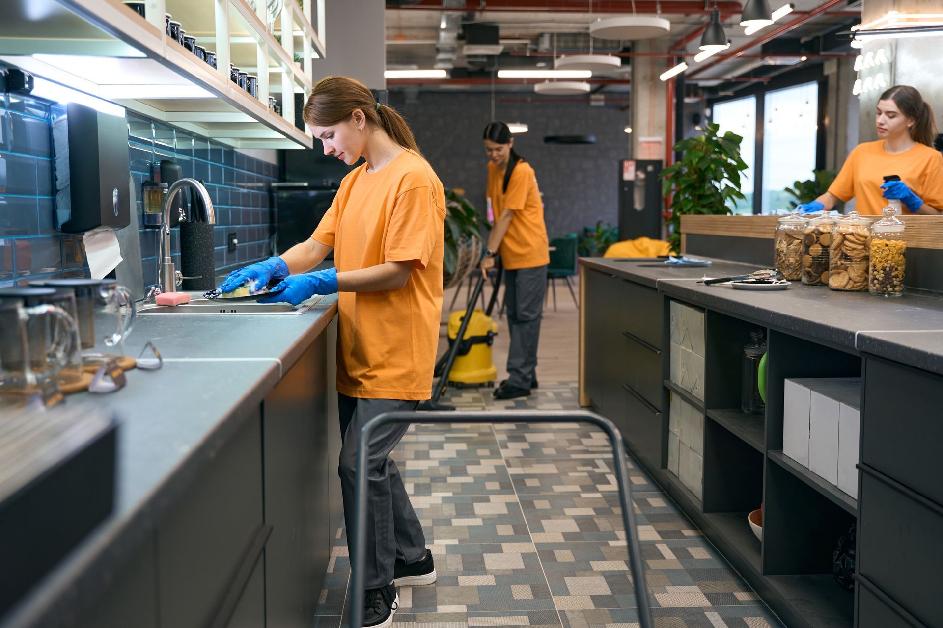 A woman is cleaning a kitchen counter with a vacuum cleaner.