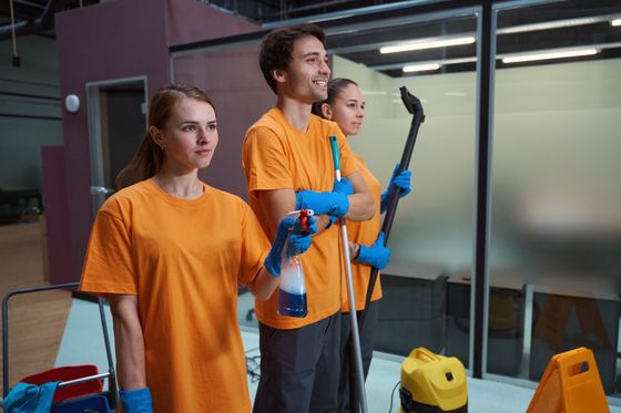 A group of janitors are standing next to each other in an office holding cleaning supplies.