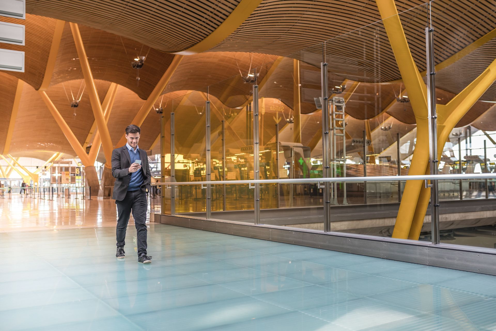 A man in a suit is standing in an airport looking at his phone.