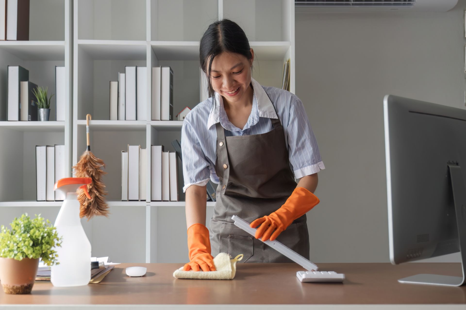 A woman wearing orange gloves is cleaning a desk in an office.