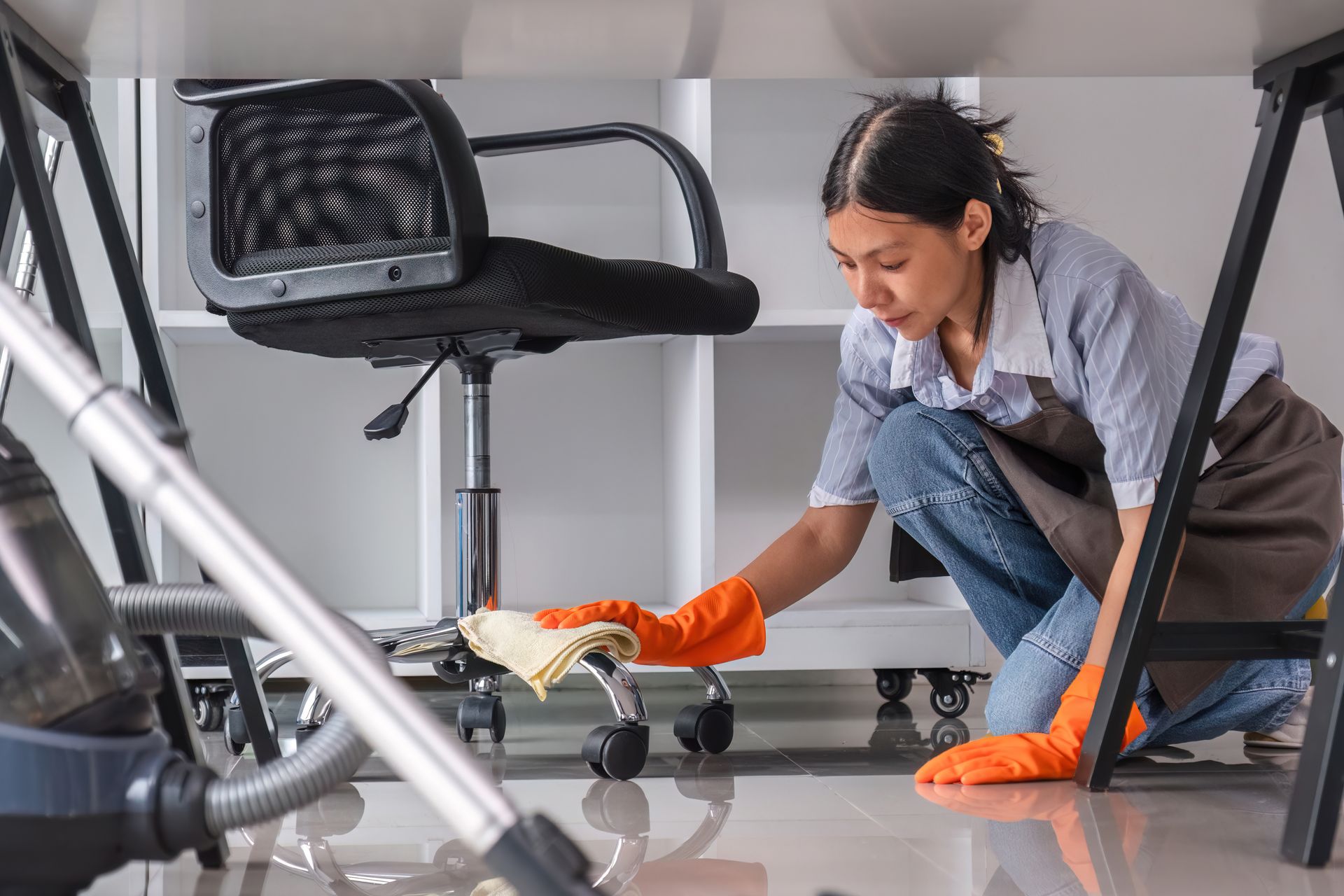 A woman is cleaning the floor of an office with a vacuum cleaner.