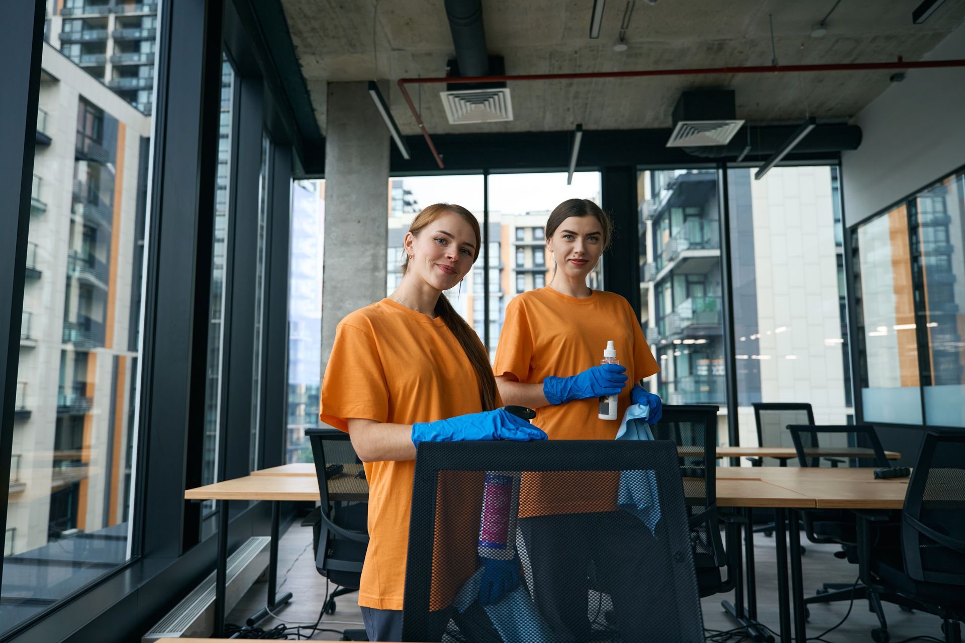 Two people in orange shirts and blue gloves holding a tray in a modern office break area