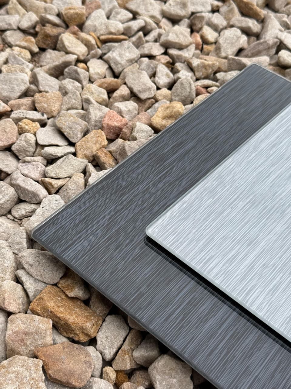 Dos placas rectangulares de metal cepillado, una gris oscuro y otra plateada, sobre un lecho de pequeñas rocas.