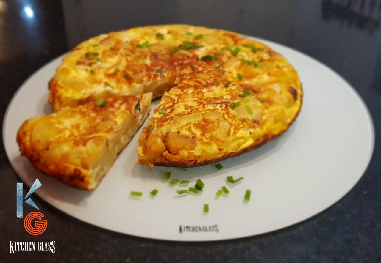 Tortilla española con una rebanada recortada, sobre un plato blanco, espolvoreada con cebollino.