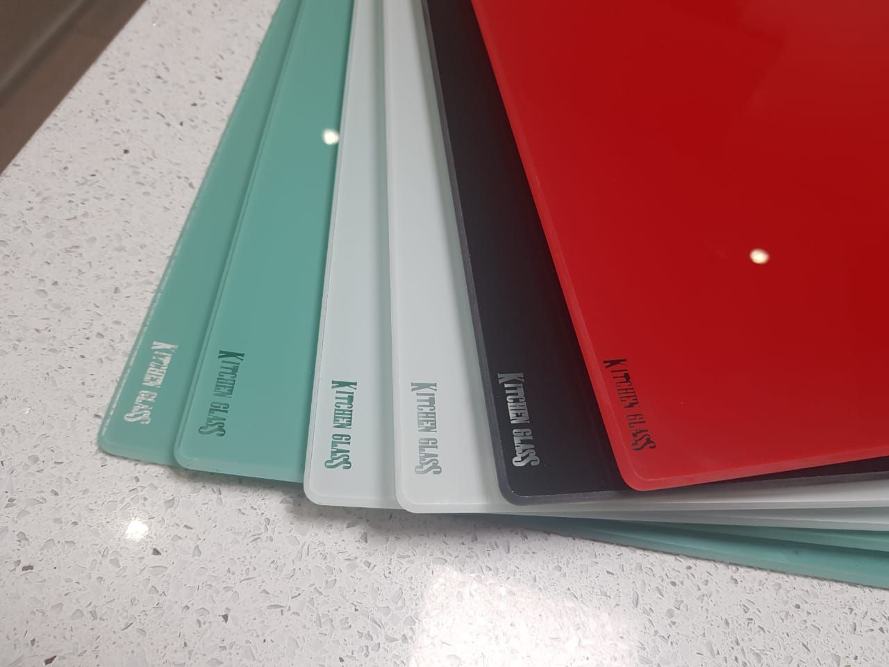 Pila de muestras de vidrio de colores sobre una encimera moteada; los colores varían del verde azulado al rojo.