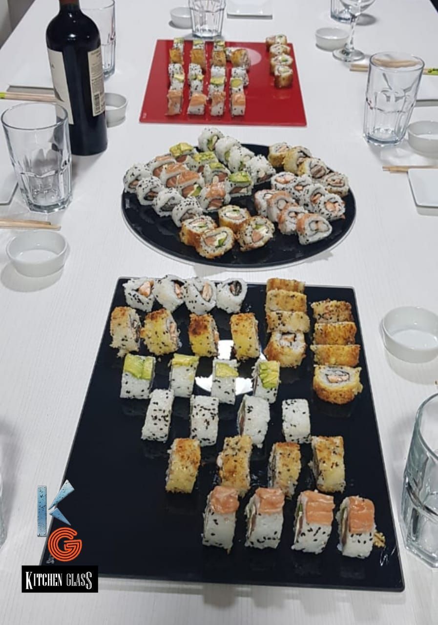 Platos de sushi en una mesa con copas de vino, palillos y platos pequeños.