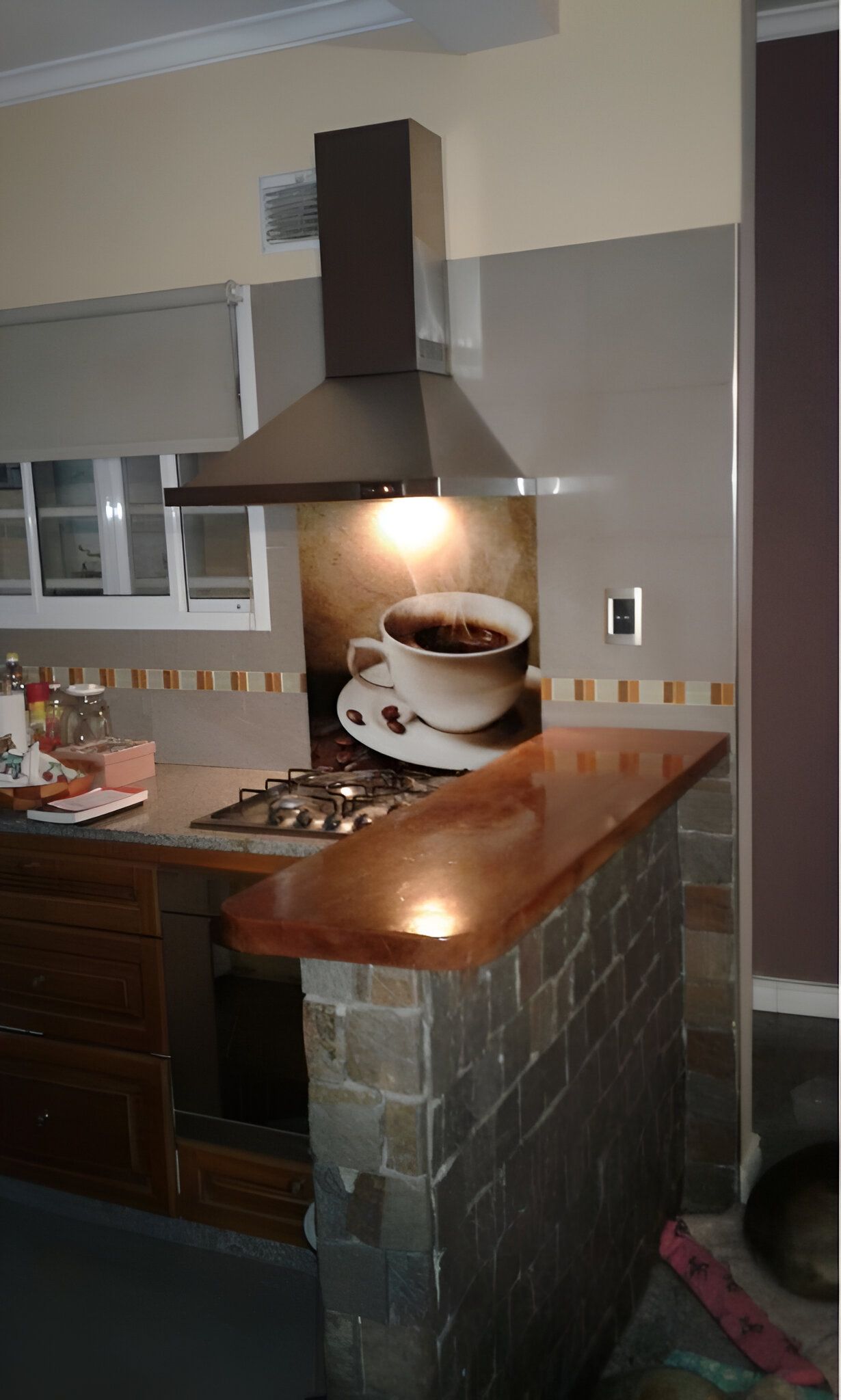 Cocina con campana marrón, encimera de madera, ladrillo de piedra y arte en forma de taza de café.