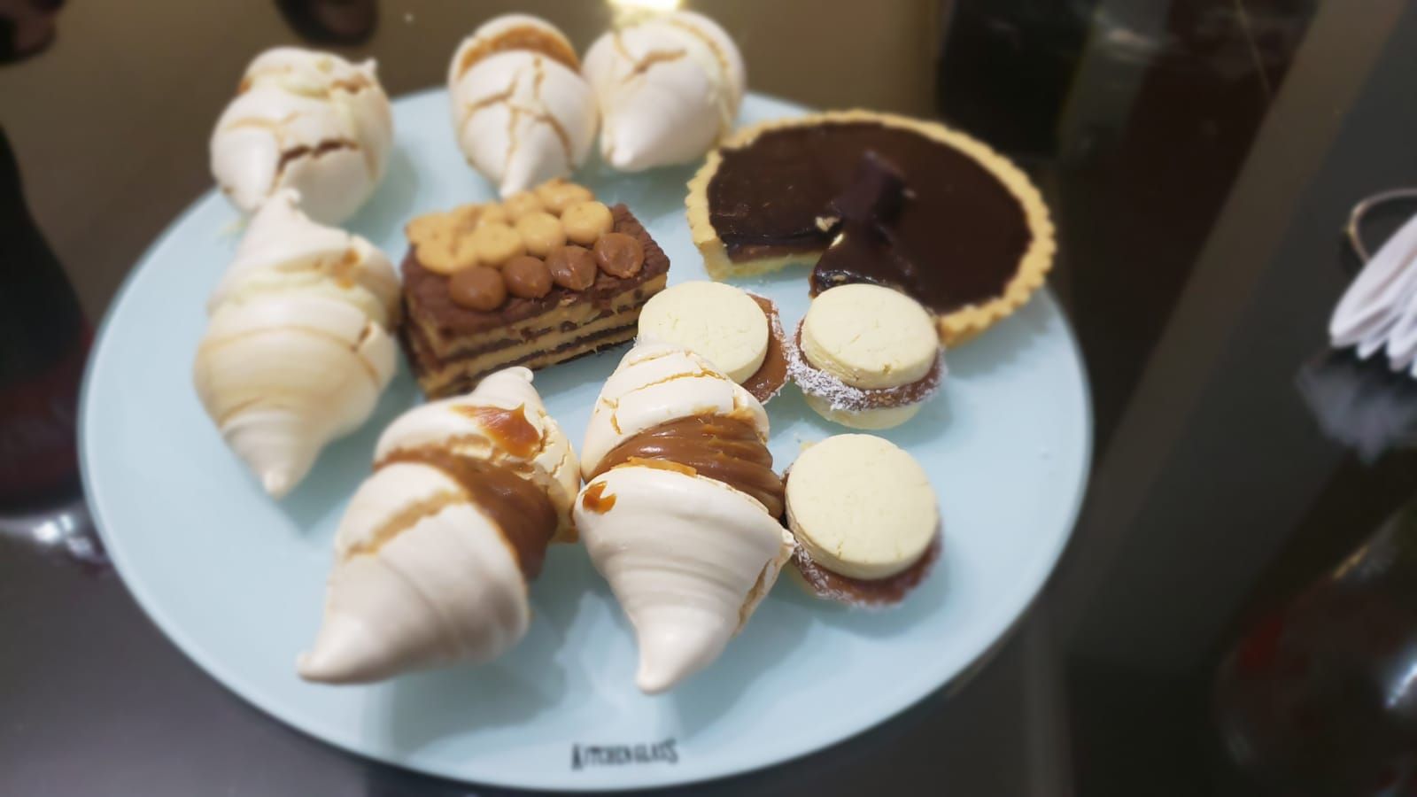 Un plato de postres variados: merengues, tarta y alfajores, en un ambiente de restaurante.