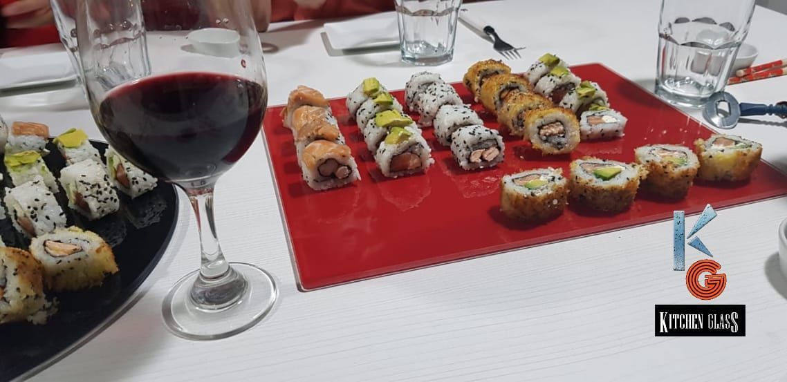 Plato de sushi y vino tinto sobre una mesa blanca.