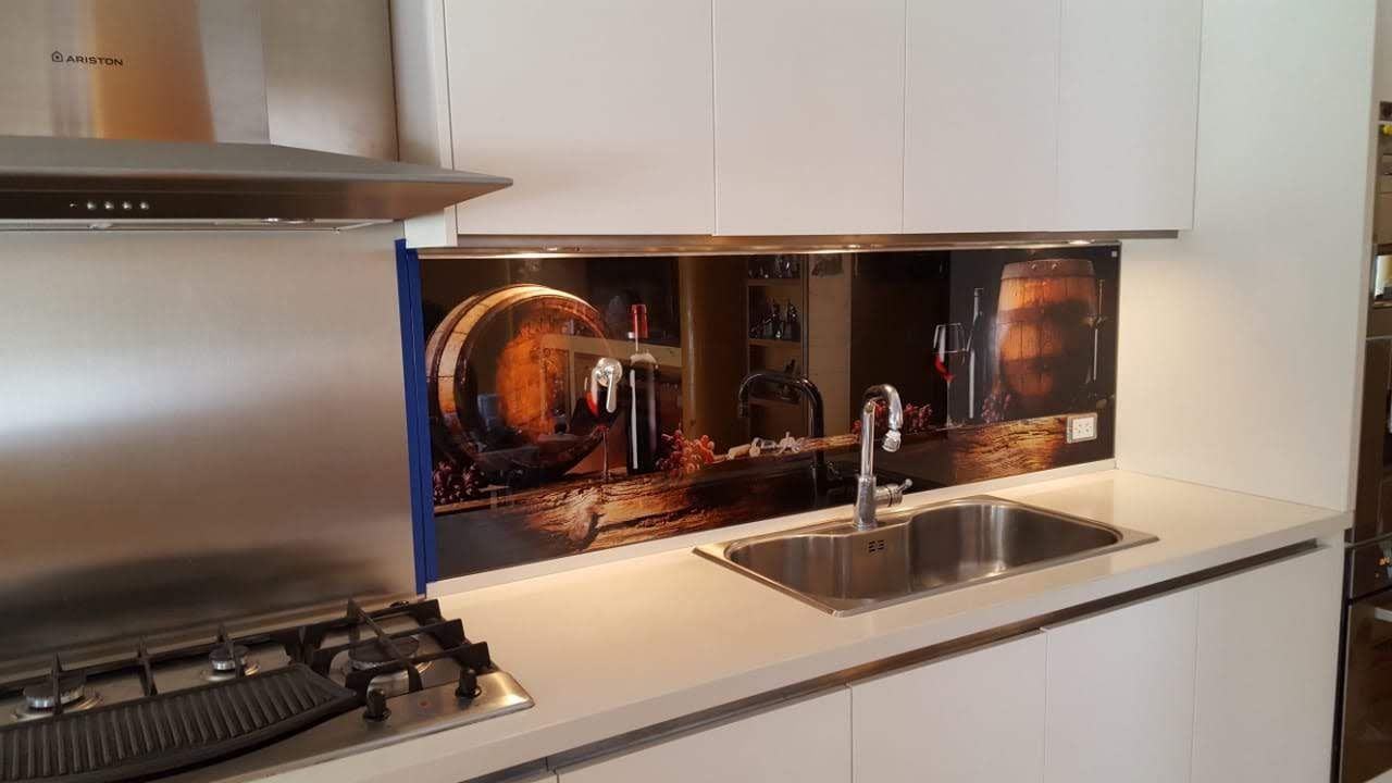 Cocina con gabinetes blancos y salpicadero de vidrio con una escena de bodega. Electrodomésticos de acero inoxidable.