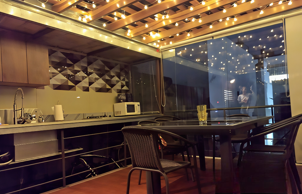Cocina al aire libre con luces de cadena, una mesa y sillas junto a una ventana.