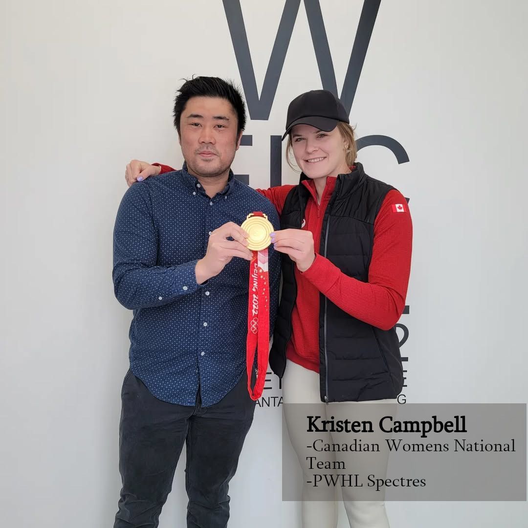 Two people stand before a logo holding an Olympic gold medal. The person on the right as Kristen Campbell.