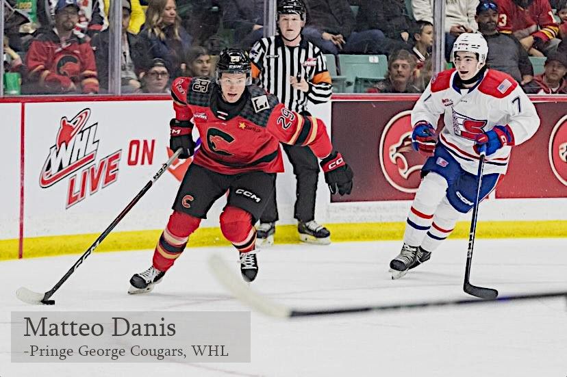 Prince George Cougars hockey player in a red jersey skates with the puck while an opposing player pursues on ice.