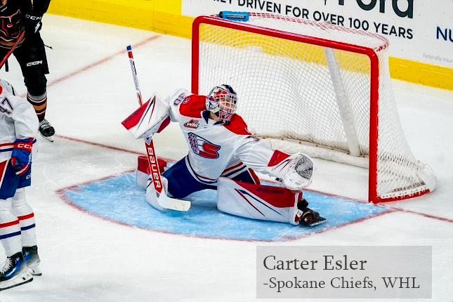 A goalie for the Spokane Chiefs in white and red gear makes a save in front of the net on an ice hockey rink.