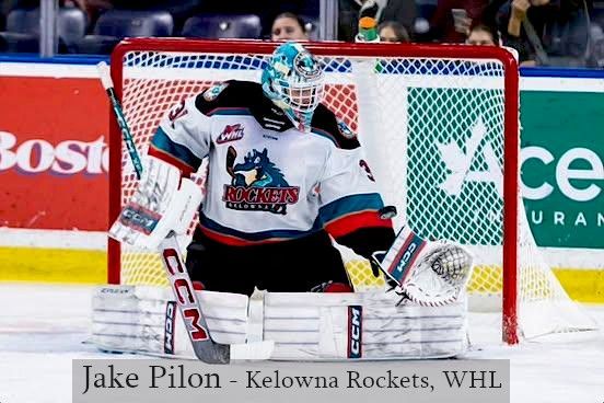 Kelowna Rockets goalie Jake Pilon in a white and teal jersey, kneeling in front of the net in a hockey arena.