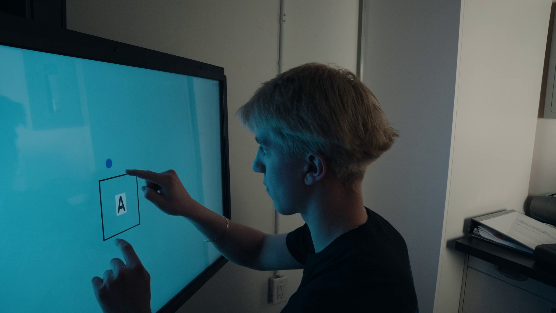 A person touches a screen displaying a hand-drawn box with the letter A inside, while a small blue dot sits above it.