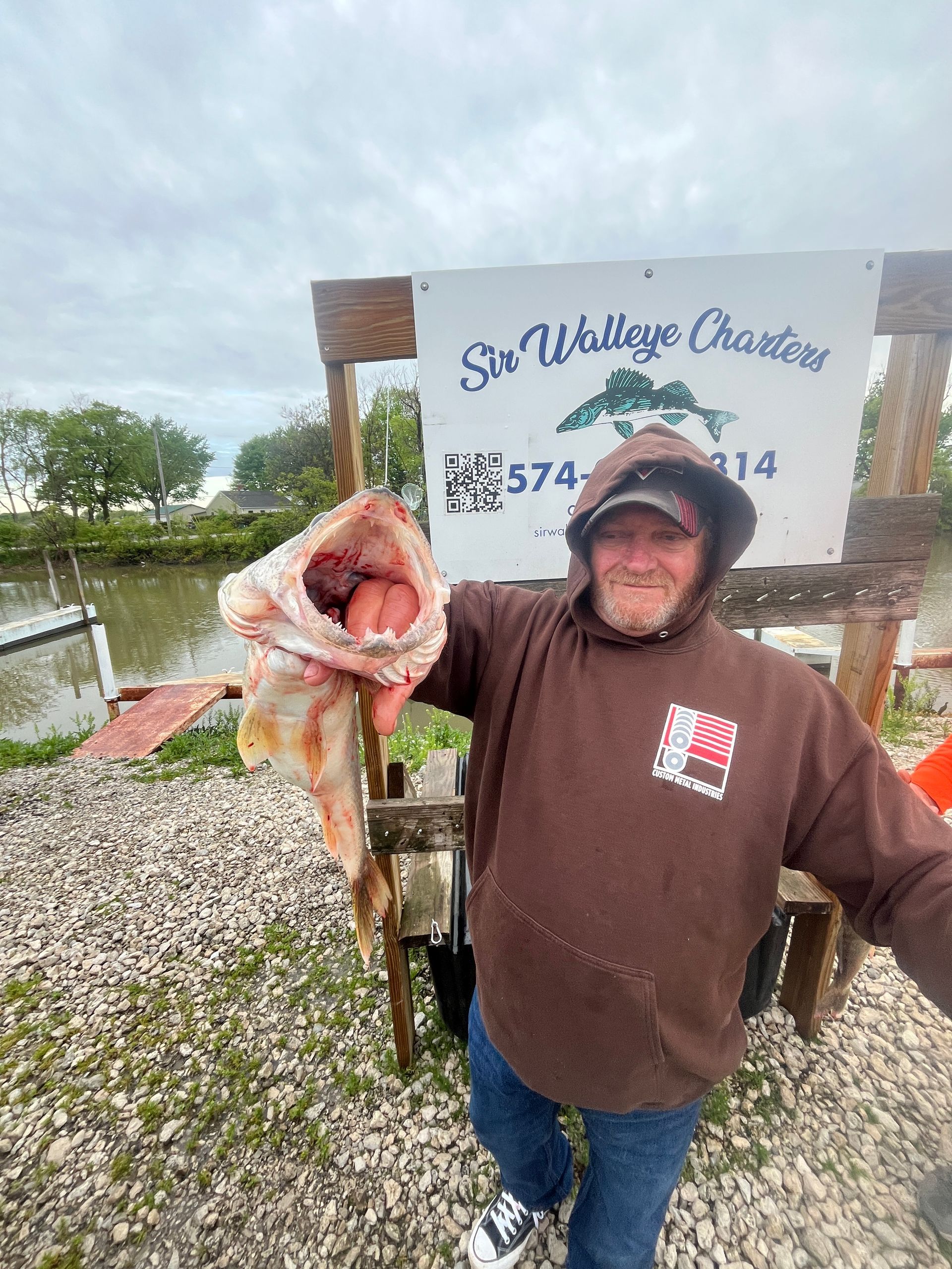 Man holding a Lake Erie Walleye showing its teeth with the Sir Walleye Charters sign in the back. 