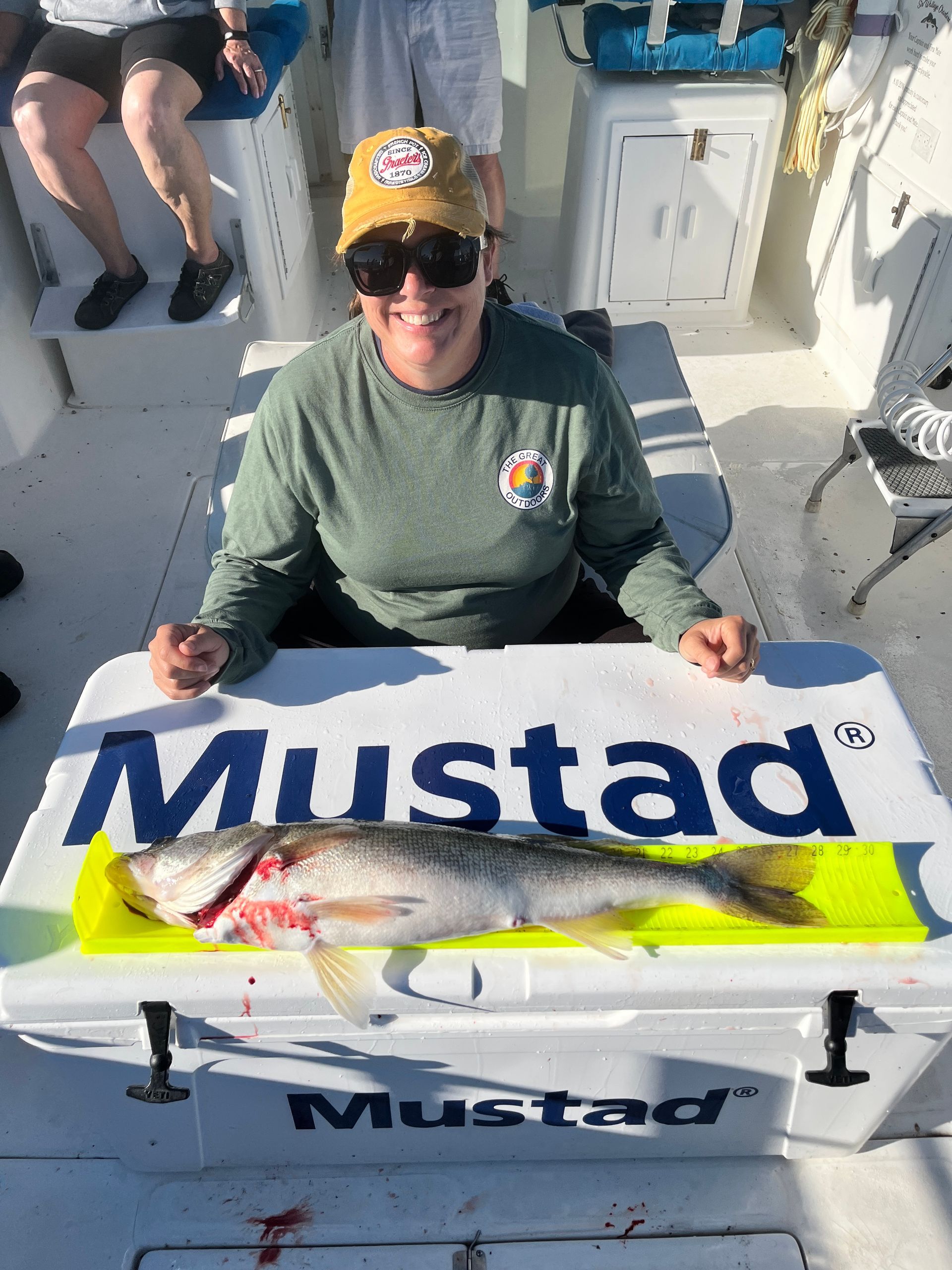 Women kneeling behind the color  with a Fish Ohio caught on Sir Walleye charters. Mustad Fishing logo is on the cooler lid.