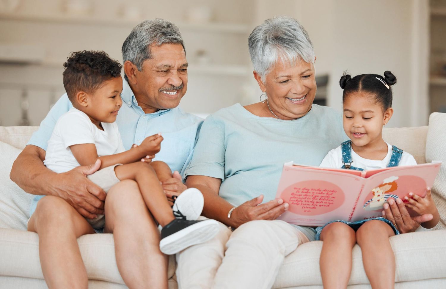 Grandparents reading to grandchildren on a couch. Book open, smiles, light setting.