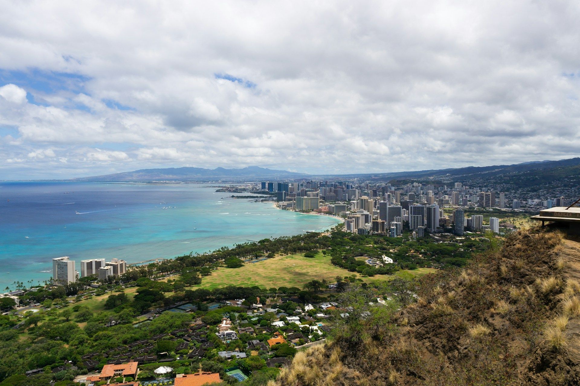 View of Waikiki city skyline and turquoise ocean under a cloudy sky.