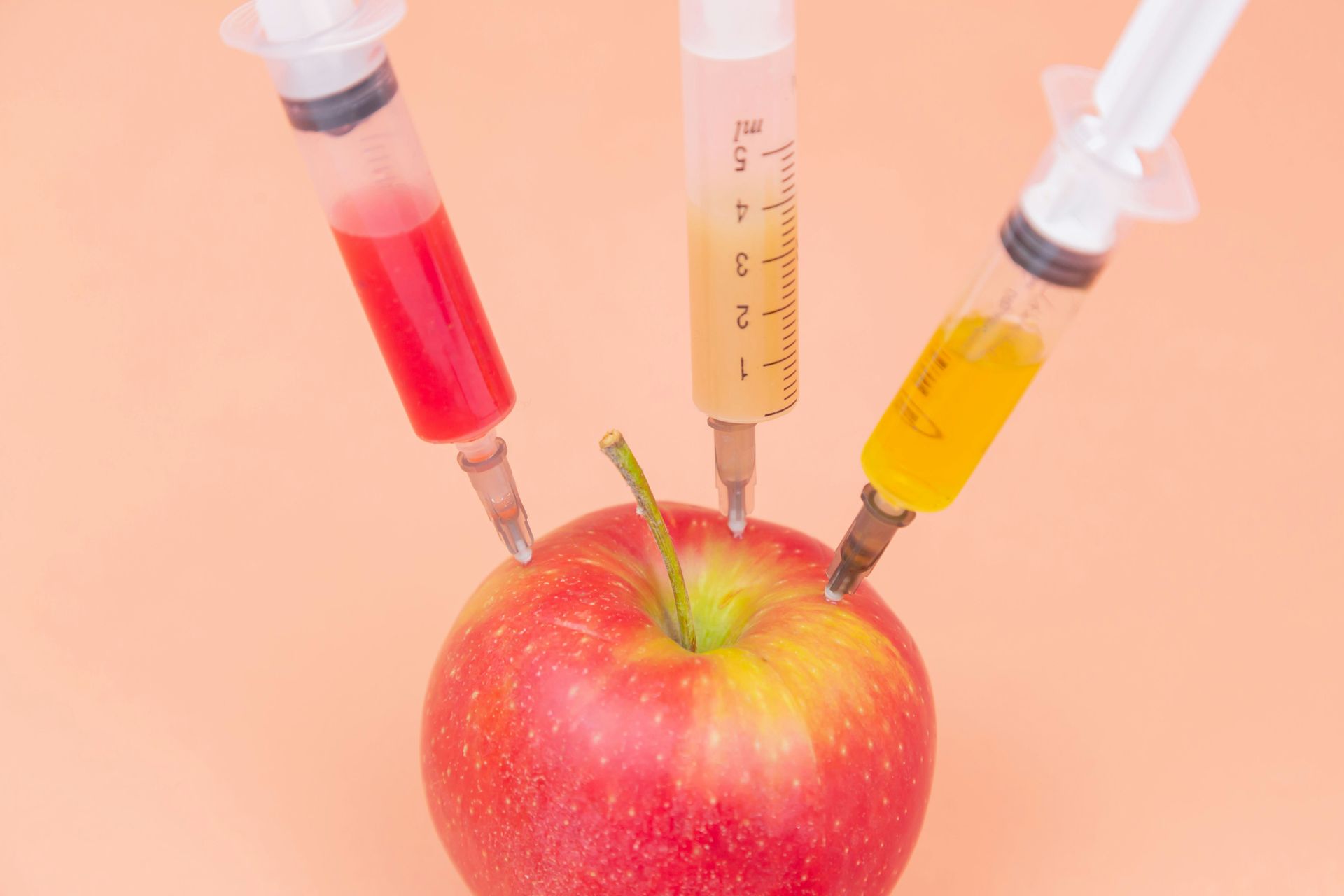 A red apple with three syringes sticking out of it.