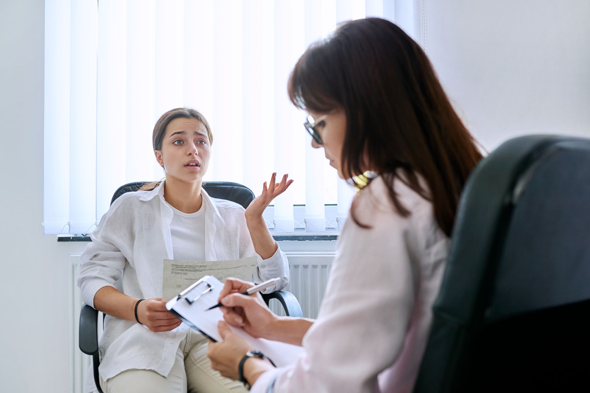 A woman is sitting in a chair talking to a doctor.