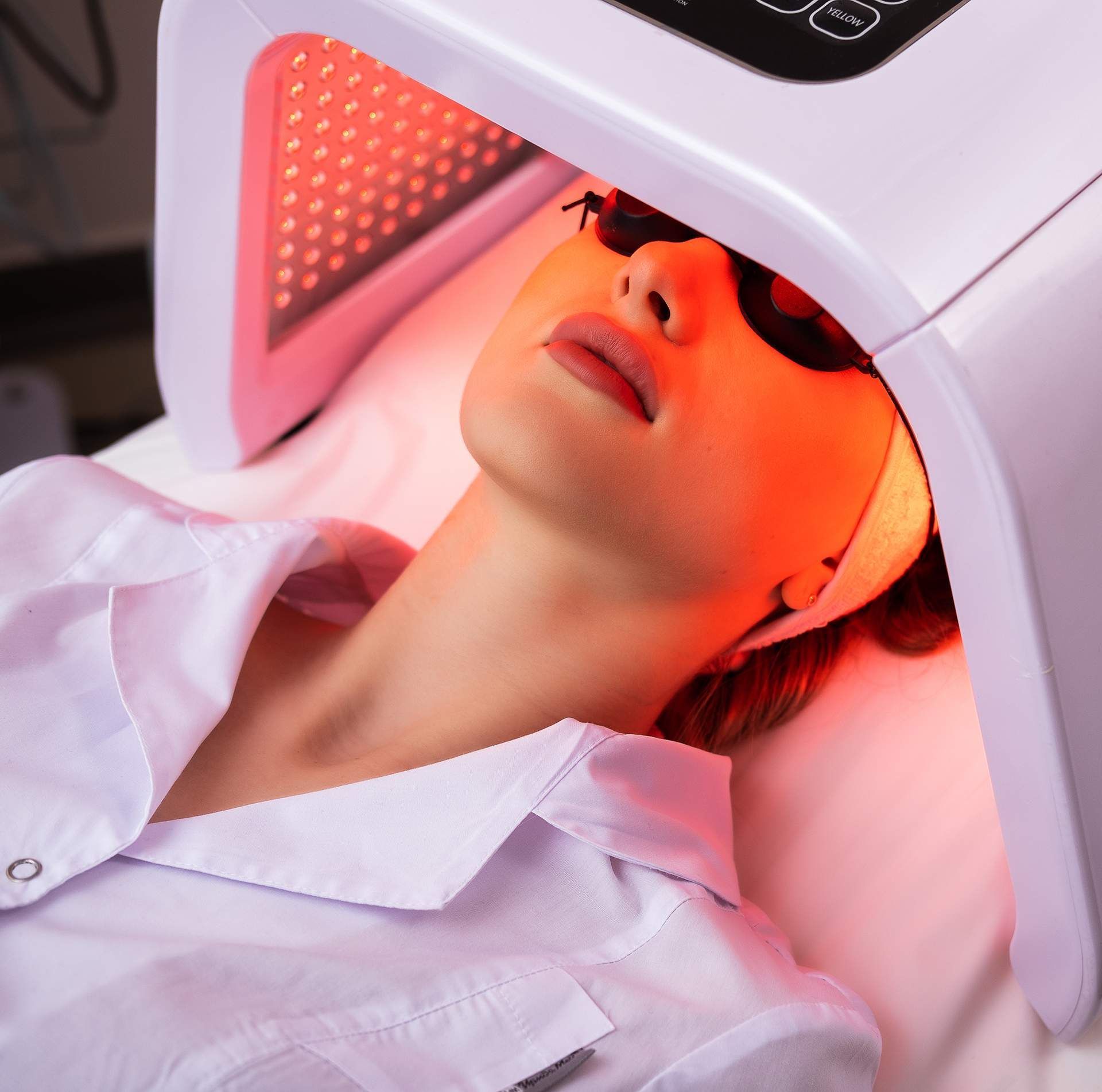A woman is laying on a bed with a red light on her face.