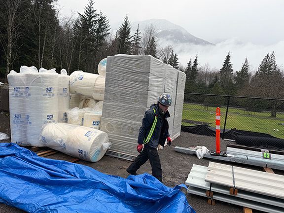 A person in safety gear walks past stacks of construction insulation and building materials.