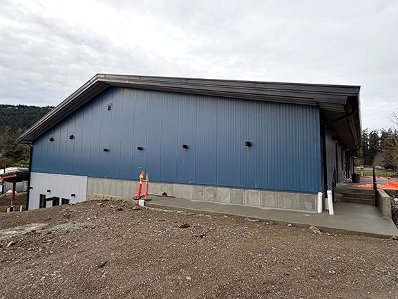 Blue and grey metal wall panels supported by concrete foundation on a hilly Ganges, BC job site.