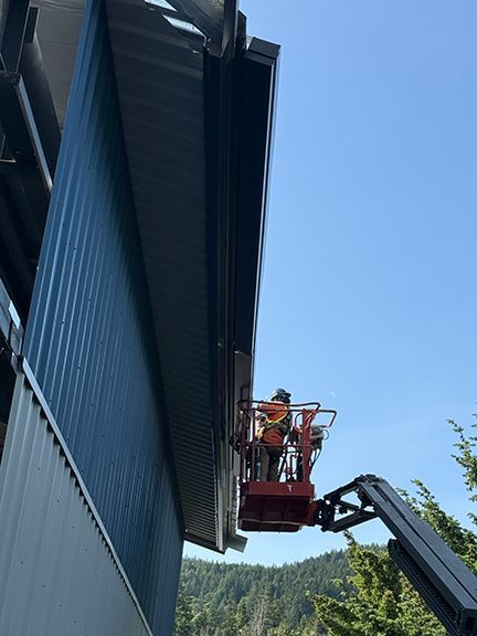 Crane lifts tradespeople to install eves troughs on metal building in BC.