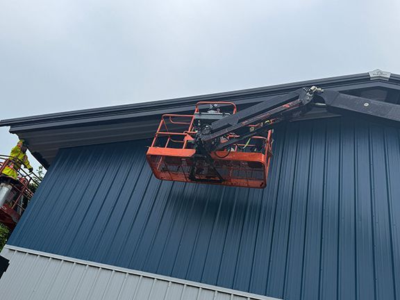 Skilled trades person using crane to install metal wall panel.