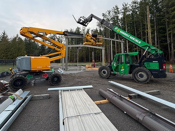 Two construction lifts work on a metal frame structure in Squamish, BC.
