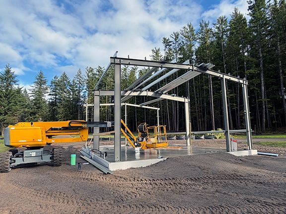 Framing at a steel building site under assembly atop a concrete foundation.
