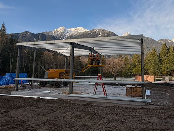 Construction workers on an elevated lift install steel roof panels on an open-frame building.