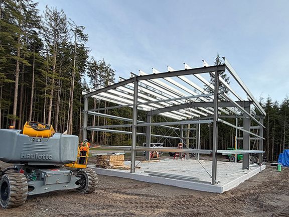 A construction site with a steel building frame being erected on a concrete foundation.