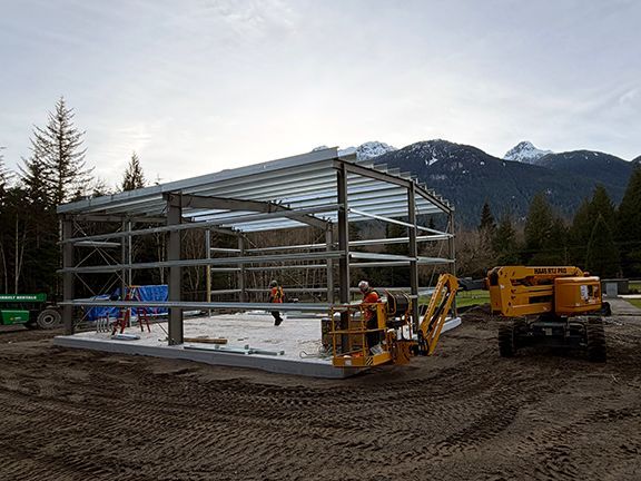 Workers construct the steel frame of a building in the mountainous setting of Squamish.