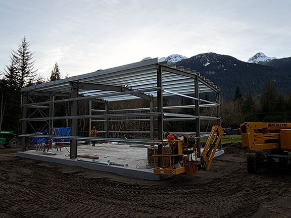 Construction of a steel-framed building with a yellow aerial lift in a mountain setting.